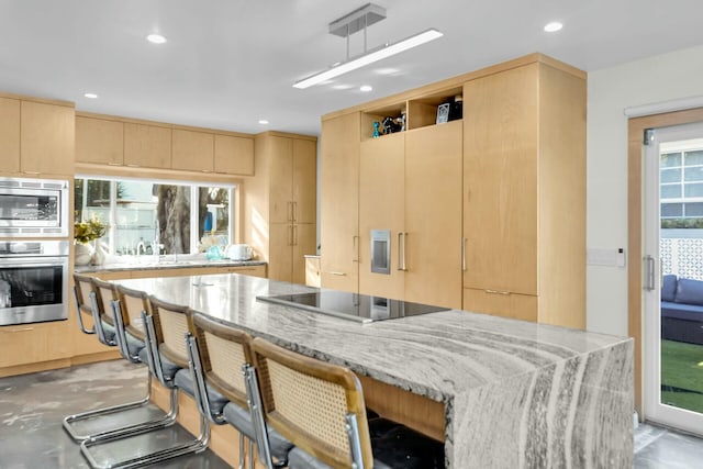 kitchen featuring light brown cabinets, a kitchen breakfast bar, appliances with stainless steel finishes, light stone countertops, and modern cabinets