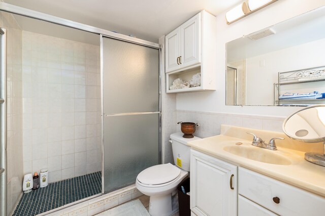 bathroom with vanity, toilet, a shower with shower door, and tile walls