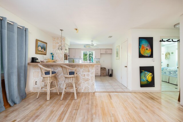 kitchen with a breakfast bar, pendant lighting, kitchen peninsula, ceiling fan, and light hardwood / wood-style floors