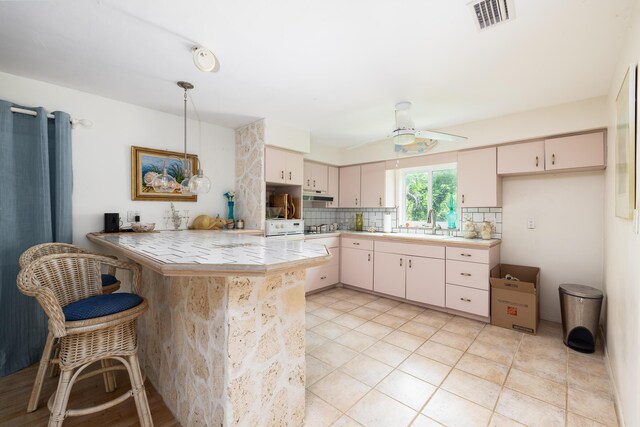 kitchen with pendant lighting, backsplash, tile counters, kitchen peninsula, and cream cabinets