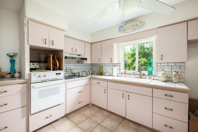 kitchen featuring sink, white cabinetry, backsplash, tile counters, and oven