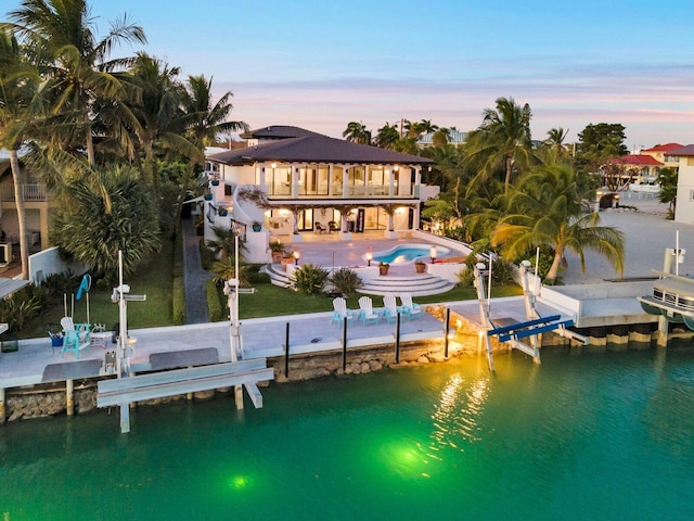 back house at dusk with a water view, a balcony, and a patio