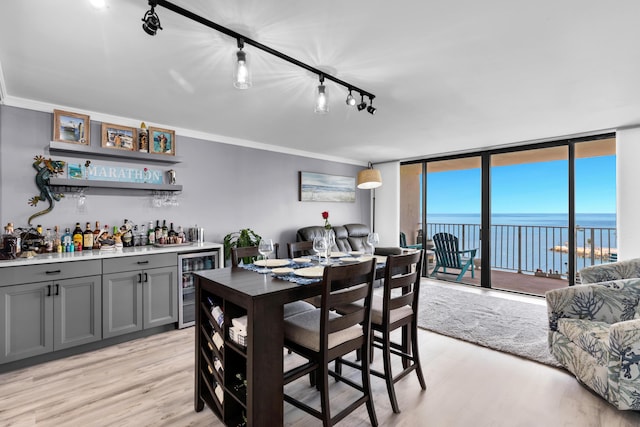 dining room with floor to ceiling windows, a water view, indoor bar, ornamental molding, and beverage cooler