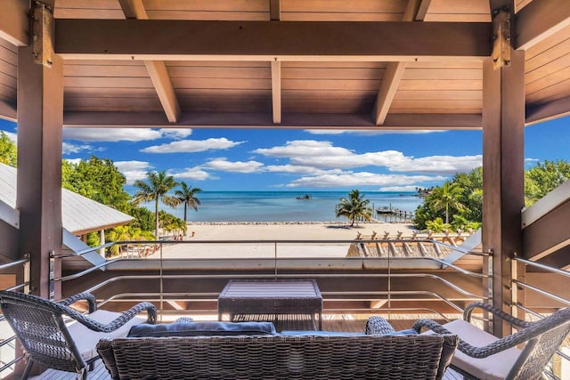 view of patio with a balcony, a water view, and a beach view