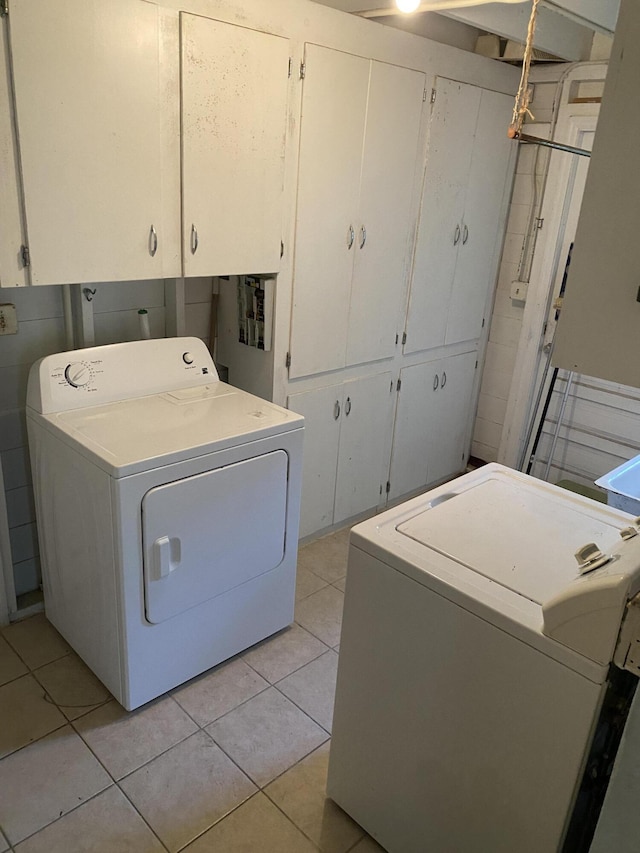 clothes washing area with washer and dryer, cabinets, and light tile patterned flooring