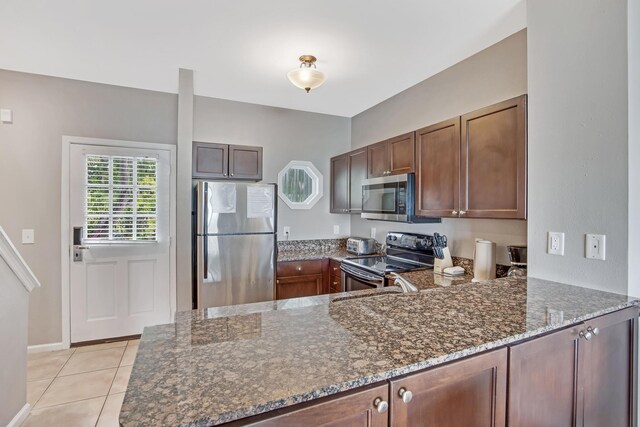 kitchen featuring light tile patterned flooring, stainless steel appliances, kitchen peninsula, and dark stone counters