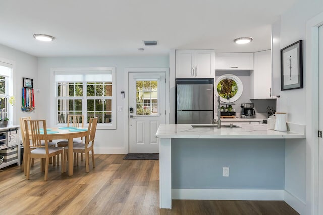 kitchen with a peninsula, visible vents, white cabinetry, plenty of natural light, and stainless steel fridge