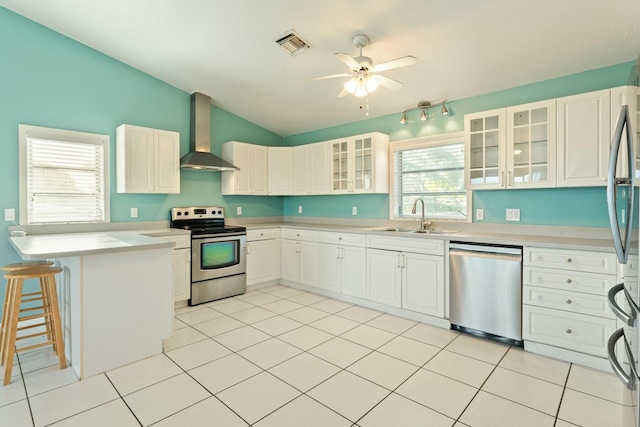 kitchen with vaulted ceiling, white cabinetry, sink, stainless steel appliances, and wall chimney exhaust hood