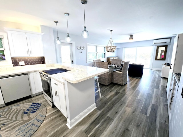 kitchen with a wall unit AC, decorative backsplash, appliances with stainless steel finishes, white cabinetry, and a peninsula