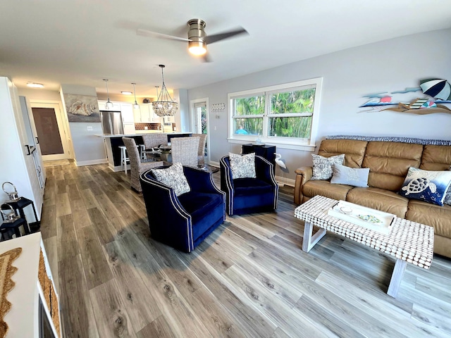 living area featuring light wood-style floors, baseboards, and ceiling fan with notable chandelier