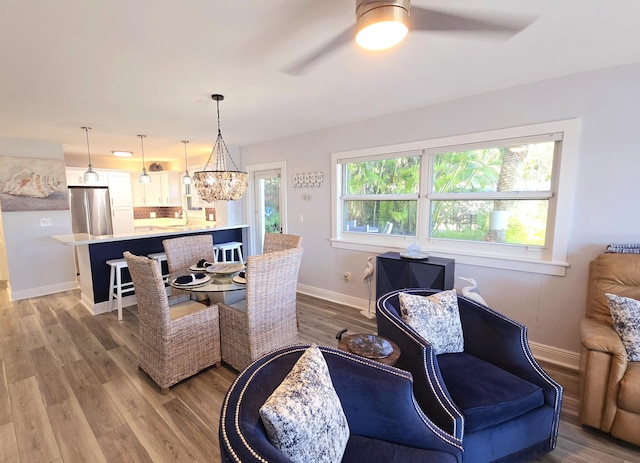 living area with ceiling fan with notable chandelier, light wood-style flooring, and baseboards