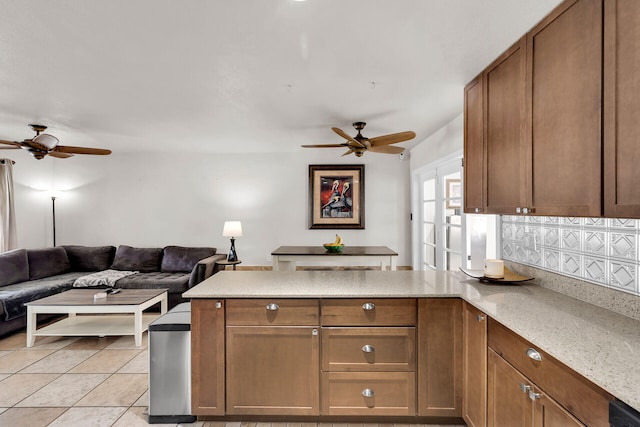 kitchen featuring light tile patterned flooring, ceiling fan, kitchen peninsula, and light stone countertops