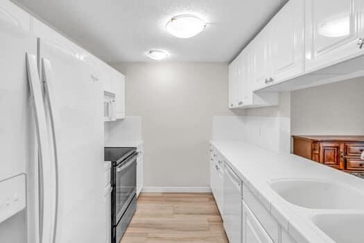 kitchen featuring white appliances, sink, light wood-type flooring, and white cabinets