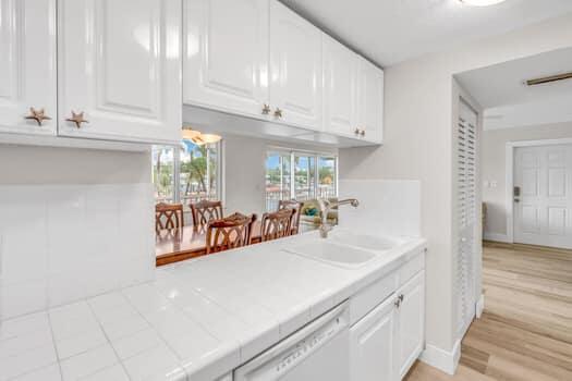 bar with sink, dishwasher, white cabinetry, light hardwood / wood-style floors, and tile countertops