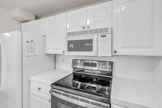 kitchen featuring tasteful backsplash, white appliances, tile counters, and white cabinets