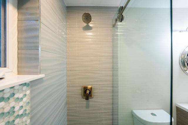 bathroom featuring stacked washer / drying machine, toilet, and a tile shower