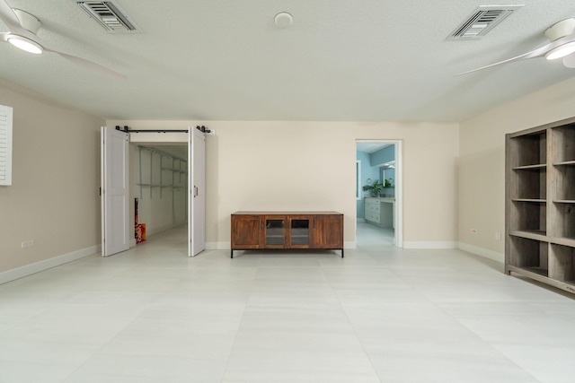 unfurnished room featuring a textured ceiling, a barn door, and ceiling fan