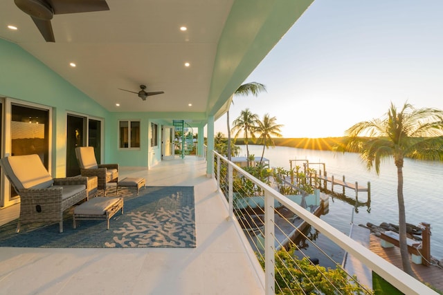 patio terrace at dusk featuring an outdoor living space, ceiling fan, and a water view