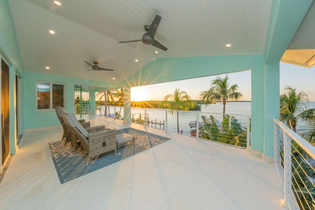 patio terrace at dusk with a bar, ceiling fan, and a water view