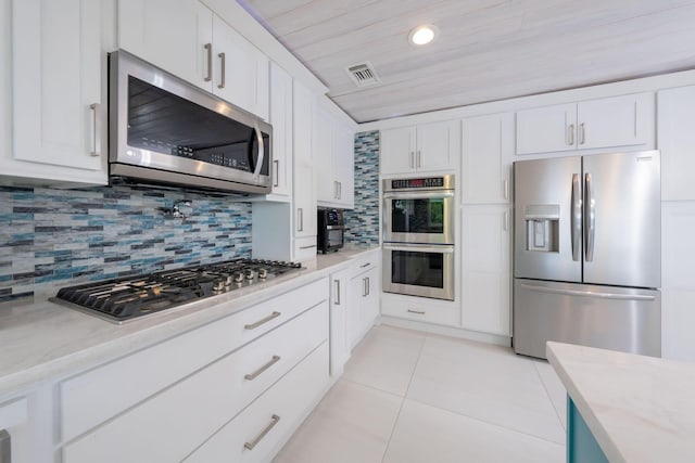 kitchen featuring stainless steel appliances, white cabinetry, light tile patterned flooring, and decorative backsplash