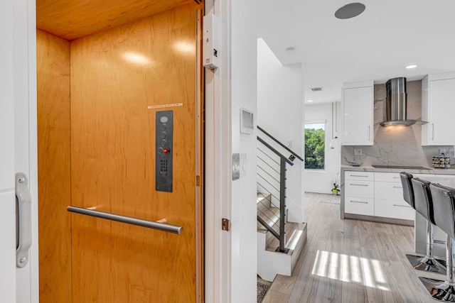 kitchen with backsplash, elevator, white cabinetry, modern cabinets, and wall chimney exhaust hood