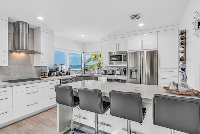 kitchen featuring a breakfast bar, visible vents, appliances with stainless steel finishes, wall chimney range hood, and modern cabinets