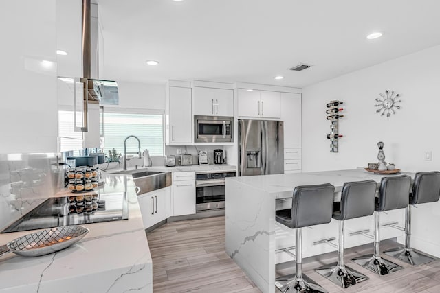 kitchen with stainless steel appliances, a peninsula, a sink, a kitchen breakfast bar, and light stone countertops