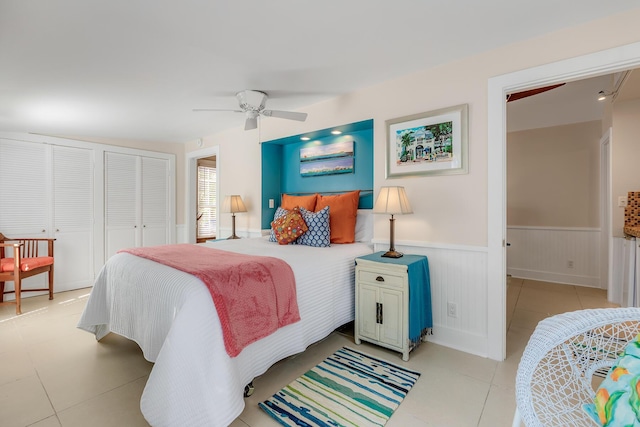 bedroom with a wainscoted wall, ceiling fan, light tile patterned floors, and a closet