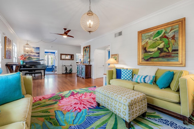 living area featuring visible vents, ornamental molding, wood finished floors, and ceiling fan with notable chandelier