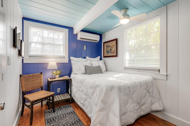 bedroom with a wall mounted AC, wood finished floors, beam ceiling, and a ceiling fan