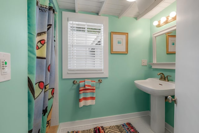 bathroom with a shower with shower curtain, beamed ceiling, a sink, and baseboards