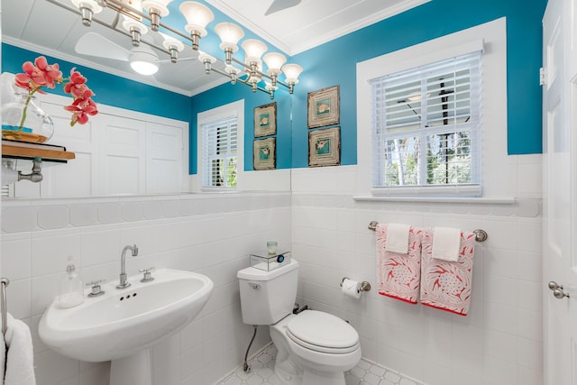 half bathroom with toilet, a wainscoted wall, a sink, crown molding, and tile walls