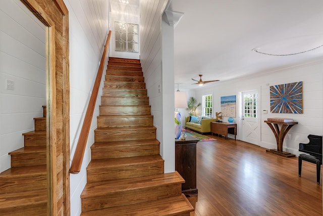 staircase with ceiling fan with notable chandelier, ornamental molding, wood walls, and wood finished floors