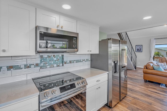 kitchen with white cabinetry, stainless steel appliances, backsplash, and light wood-type flooring