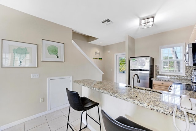 kitchen with light tile patterned floors, sink, a breakfast bar area, stainless steel appliances, and light stone countertops