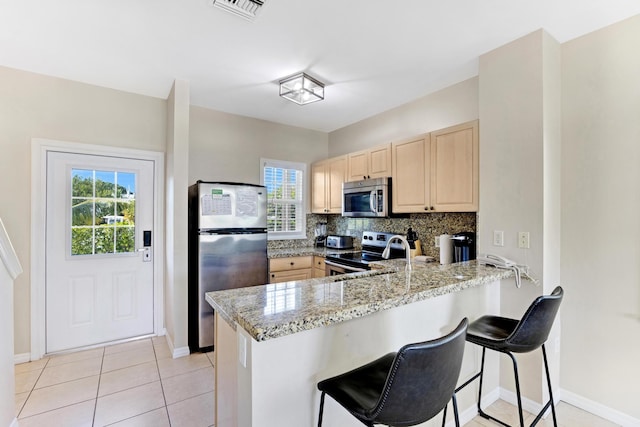 kitchen with light brown cabinetry, tasteful backsplash, light stone counters, kitchen peninsula, and stainless steel appliances