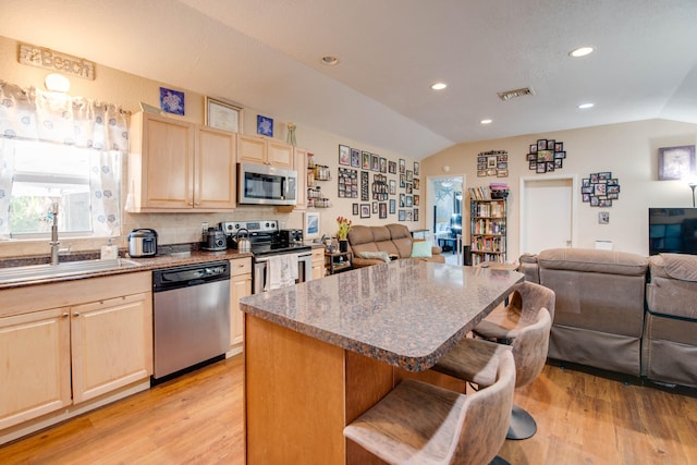kitchen with stainless steel appliances, light brown cabinets, open floor plan, and vaulted ceiling