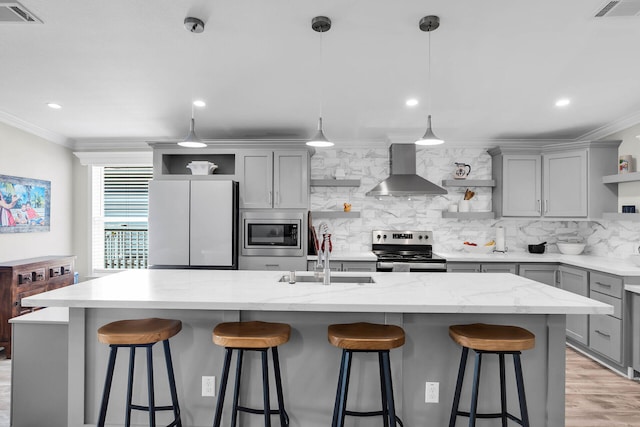 kitchen featuring a center island with sink, stainless steel appliances, wall chimney range hood, gray cabinets, and sink