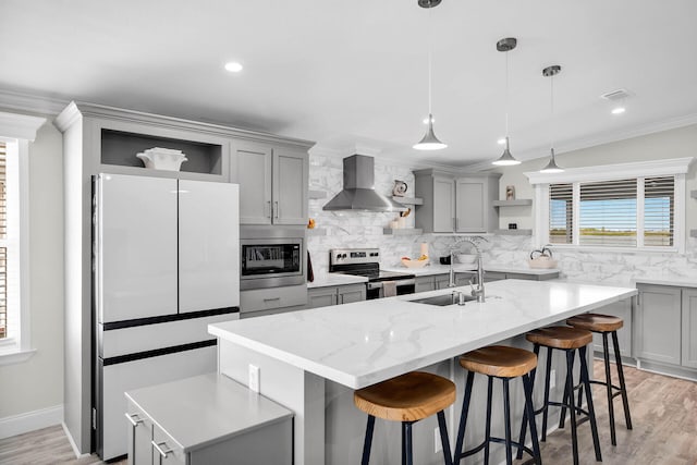 kitchen with sink, stainless steel appliances, an island with sink, and wall chimney range hood