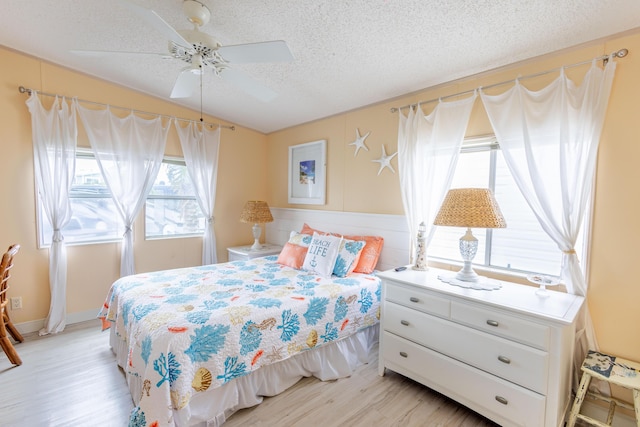 bedroom featuring ceiling fan, vaulted ceiling, a textured ceiling, and light wood-type flooring