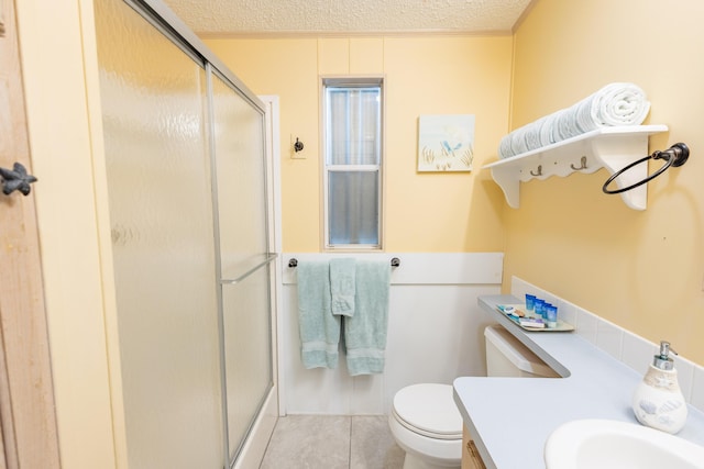 bathroom with tile patterned floors, toilet, sink, a textured ceiling, and a shower with door