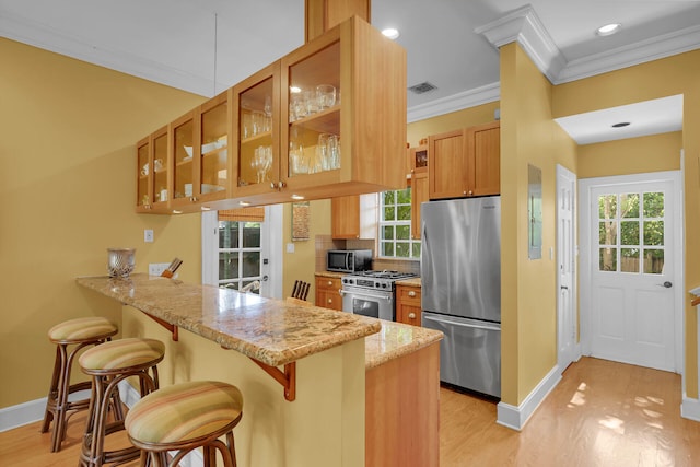 kitchen featuring glass insert cabinets, a breakfast bar area, appliances with stainless steel finishes, and a peninsula