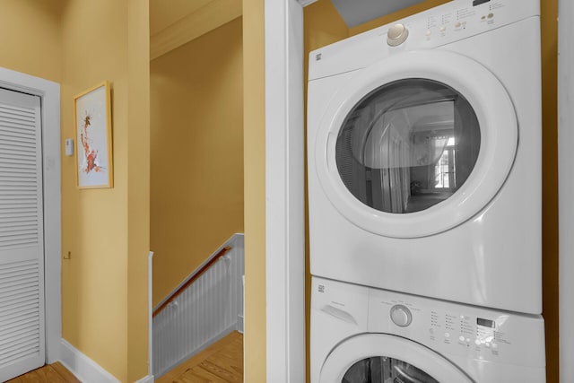 washroom featuring laundry area, light wood-type flooring, baseboards, and stacked washer / drying machine