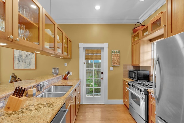 kitchen featuring crown molding, appliances with stainless steel finishes, light stone countertops, a sink, and glass insert cabinets