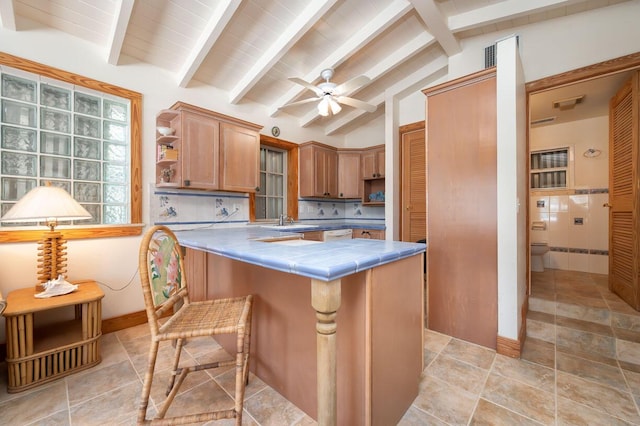 kitchen featuring tile countertops, sink, vaulted ceiling with beams, a kitchen bar, and kitchen peninsula