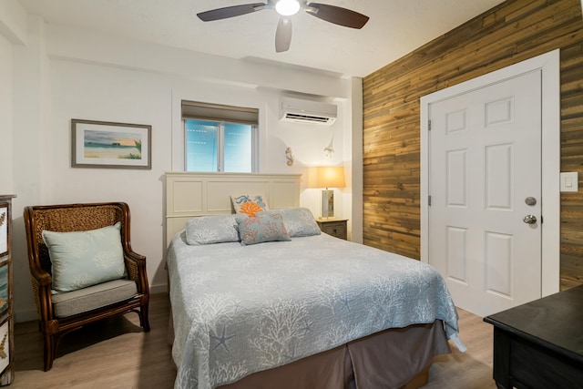 bedroom featuring a wall mounted air conditioner, hardwood / wood-style flooring, ceiling fan, and wood walls