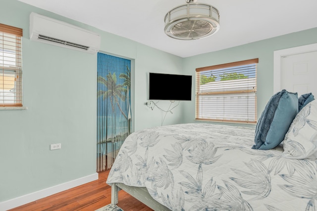 bedroom with a wall unit AC, wood finished floors, and baseboards