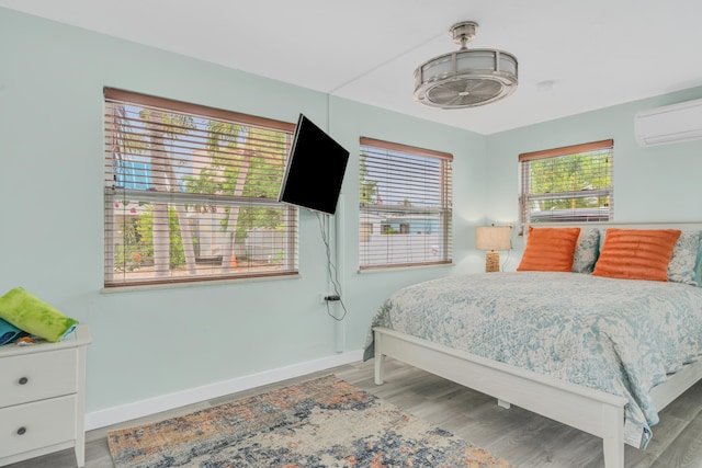 bedroom with light wood-type flooring, baseboards, and an AC wall unit