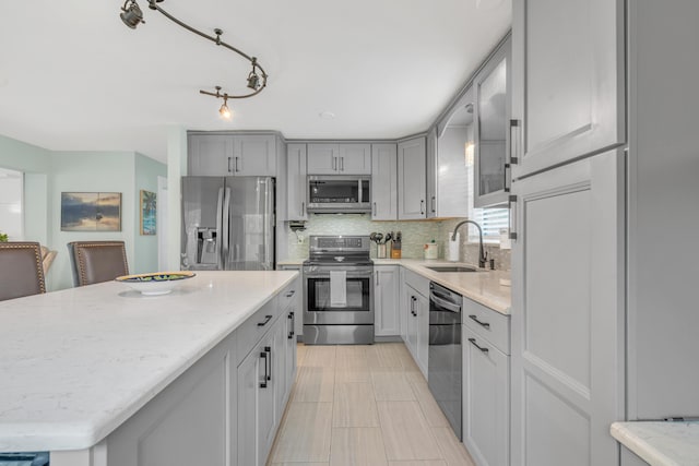 kitchen featuring light stone counters, appliances with stainless steel finishes, a center island, a sink, and backsplash