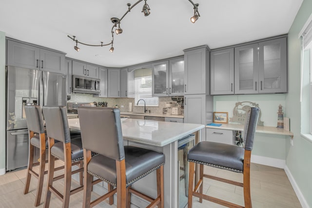 kitchen with wine cooler, backsplash, appliances with stainless steel finishes, glass insert cabinets, and a kitchen island